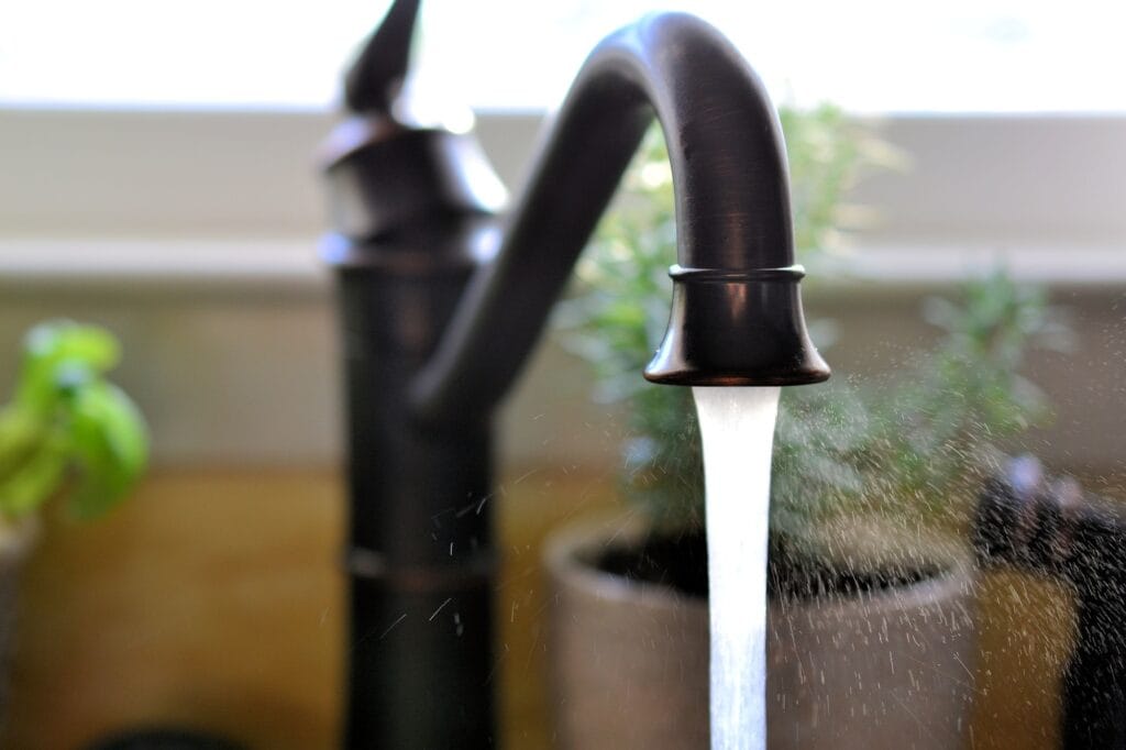 Kitchen Sink Faucet with running, spraying water with a window and herbs herb plants